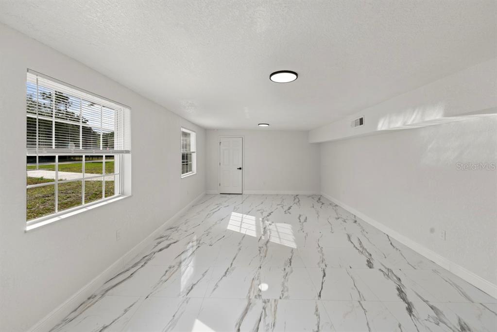 An empty room features white walls, recessed lighting, and white marble-patterned tile flooring — 1602 S TANNER ROAD, ORLANDO, FL