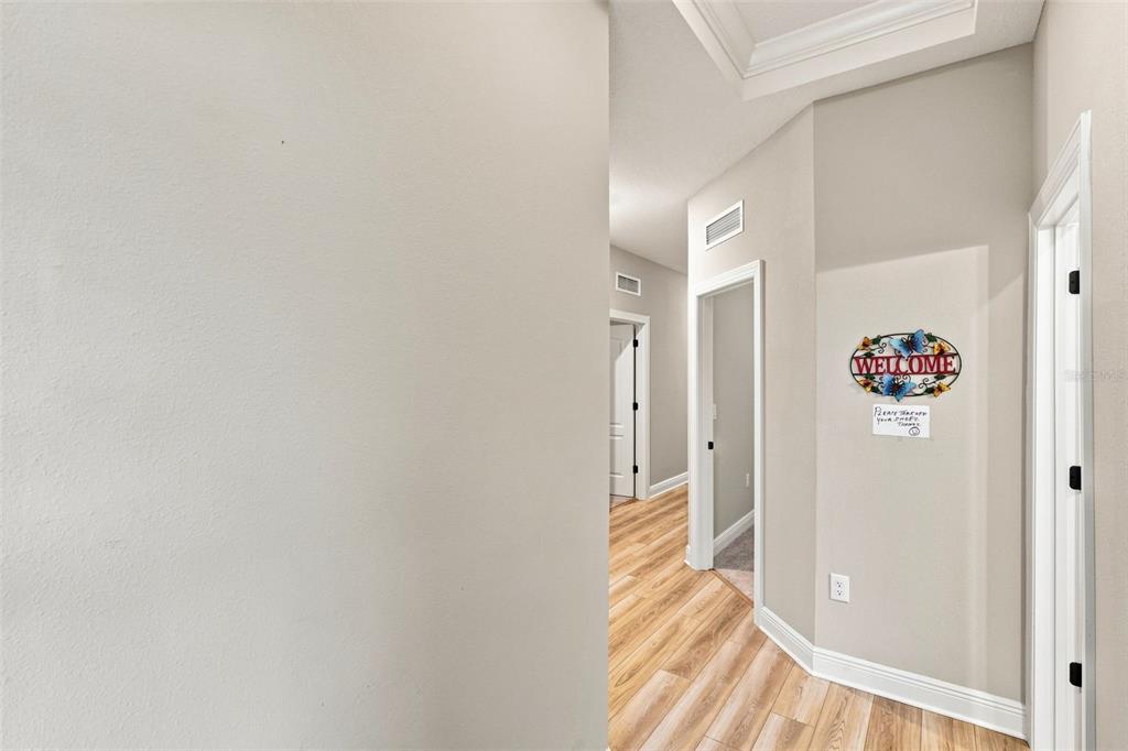 A hallway with light wood-look flooring leads to an interior room with a welcome sign — 7721 SOMERSWORTH DRIVE, KISSIMMEE, FL