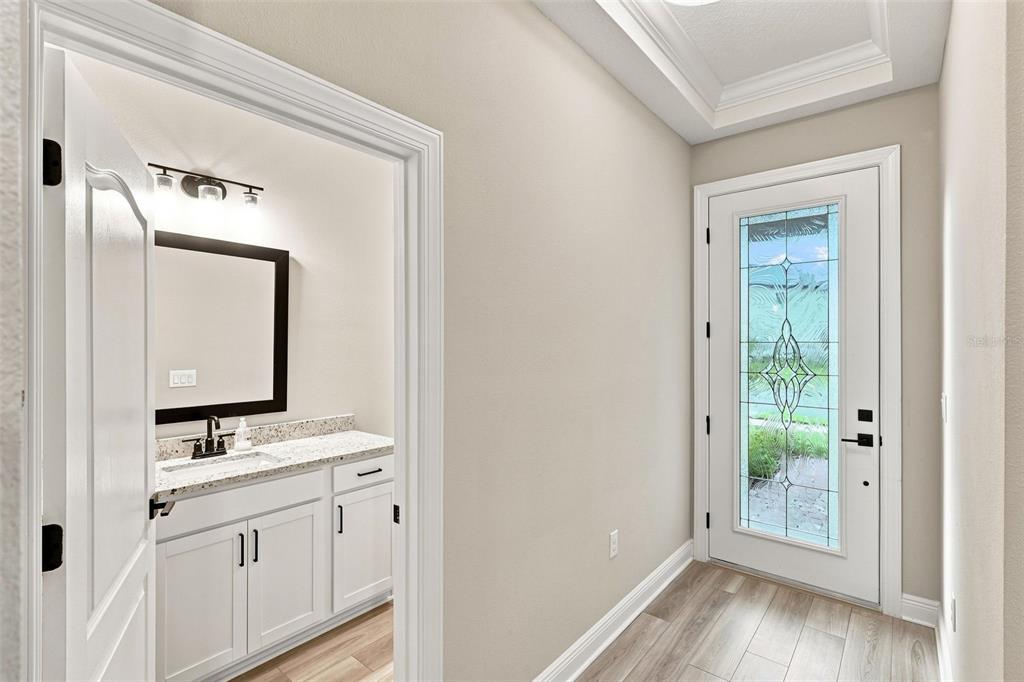 A view of a home entryway with wood-look flooring, a glass-paneled front door, and a bathroom — 7721 SOMERSWORTH DRIVE, KISSIMMEE, FL