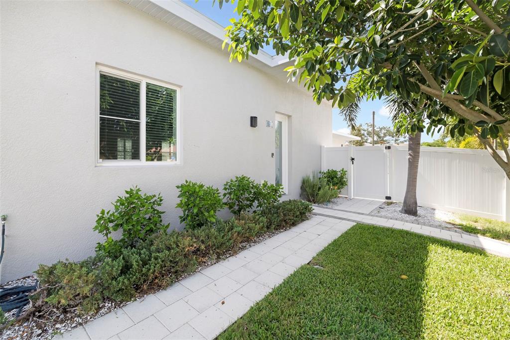 A white house exterior features a paved walkway, green landscaping, and a white privacy fence — 4524 RIVERWOOD AVENUE, SARASOTA, FL