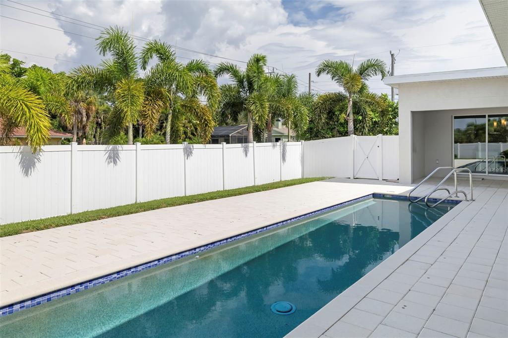 A rectangular swimming pool sits on a paved patio next to a white vinyl privacy fence — 4524 RIVERWOOD AVENUE, SARASOTA, FL