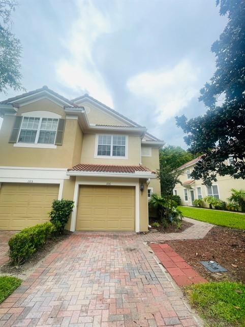 A two-story tan townhouse features a brick paver driveway and two attached garages — 3602 SHALLOT DRIVE UNIT 106, ORLANDO, FL