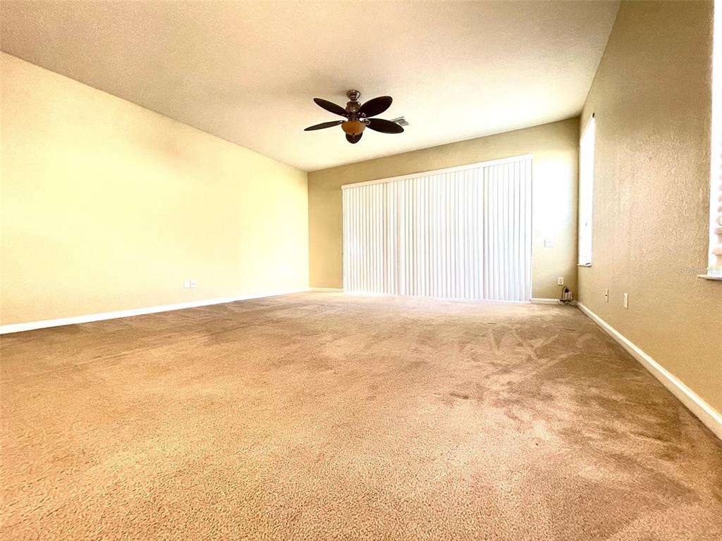 An empty living room features beige carpet, light-colored walls, a ceiling fan, and sliding glass doors — 3602 SHALLOT DRIVE UNIT 106, ORLANDO, FL