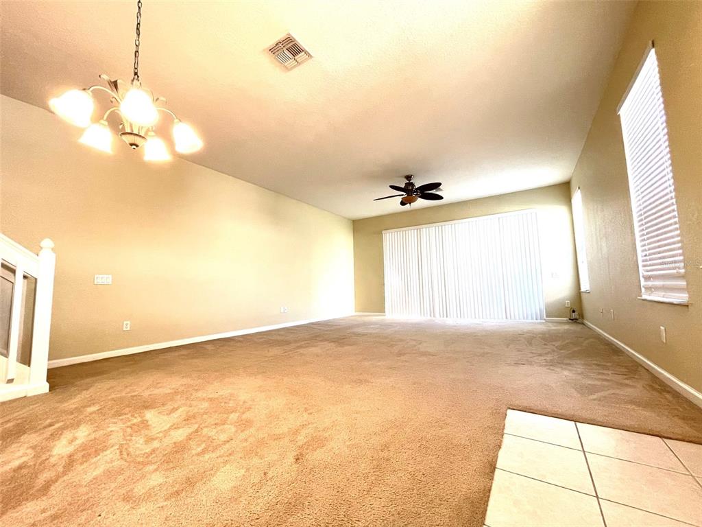 A spacious living room features beige carpeting, a chandelier, a ceiling fan, and vertical blinds — 3602 SHALLOT DRIVE UNIT 106, ORLANDO, FL