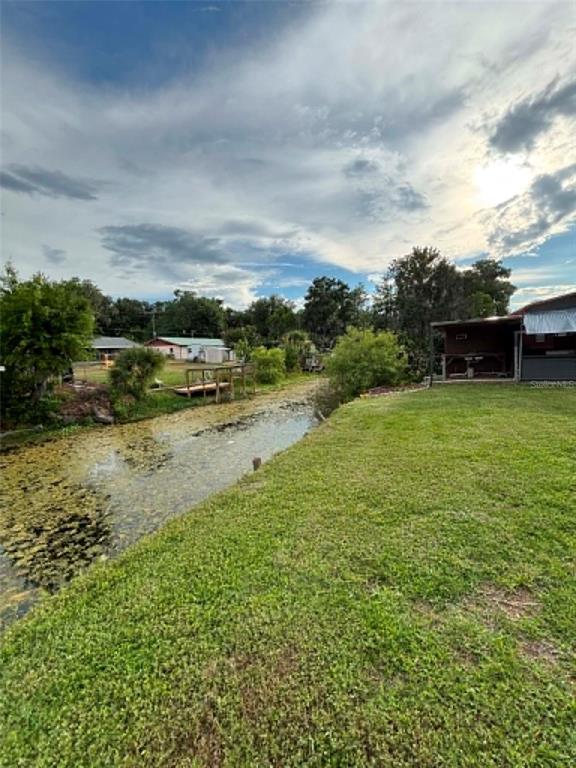 A grassy backyard features a narrow, vegetation-filled canal leading toward neighboring houses under a cloudy sky — 919 CR 482D, LAKE PANASOFFKEE, FL