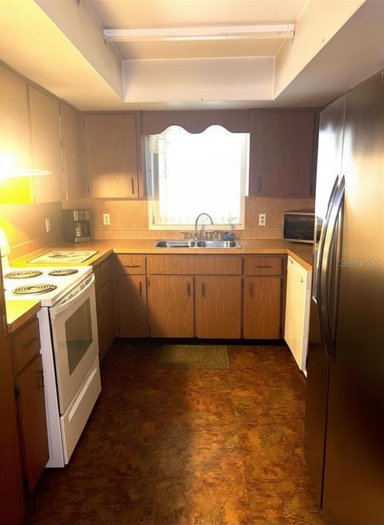 A kitchen features wood cabinets, a white stove, a stainless steel refrigerator, and linoleum flooring — 919 CR 482D, LAKE PANASOFFKEE, FL