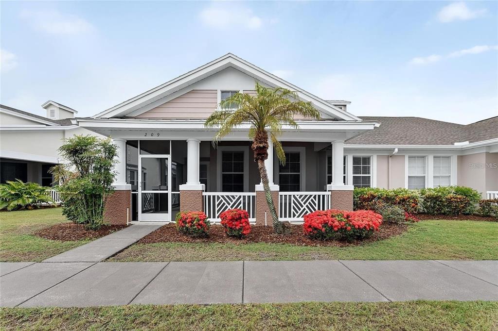 A single-story house features a covered front porch with a palm tree and red flowers — 209 SELA COVE CIRCLE, APOLLO BEACH, FL