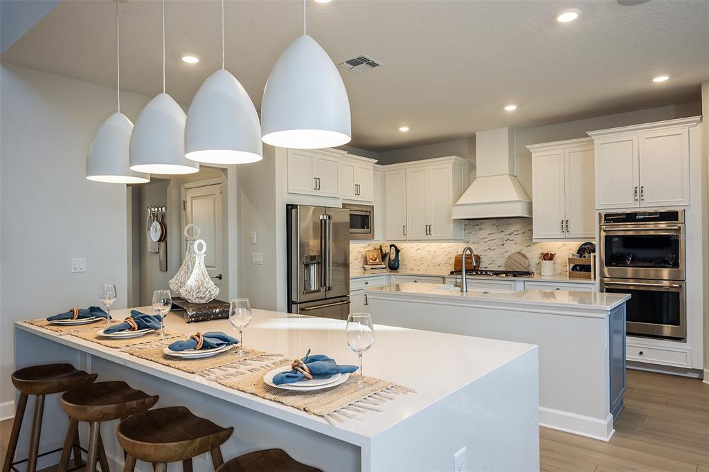 A modern kitchen features white cabinetry, a large quartz island, and four pendant lights — 19326 LOCHSIDE LANE, MOUNT DORA, FL
