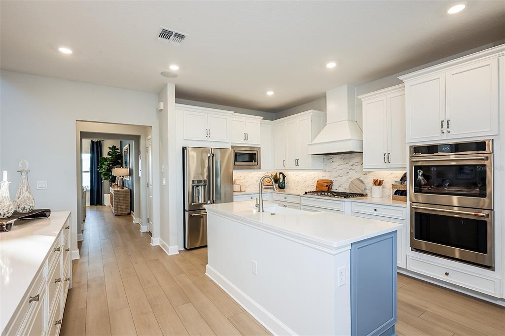 A modern kitchen features white cabinetry, stainless steel appliances, a center island, and marble backsplash — 19326 LOCHSIDE LANE, MOUNT DORA, FL