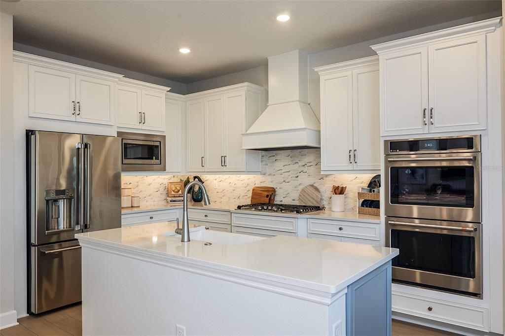A modern kitchen features white cabinetry, a blue island, stainless steel appliances, and wood flooring — 19326 LOCHSIDE LANE, MOUNT DORA, FL