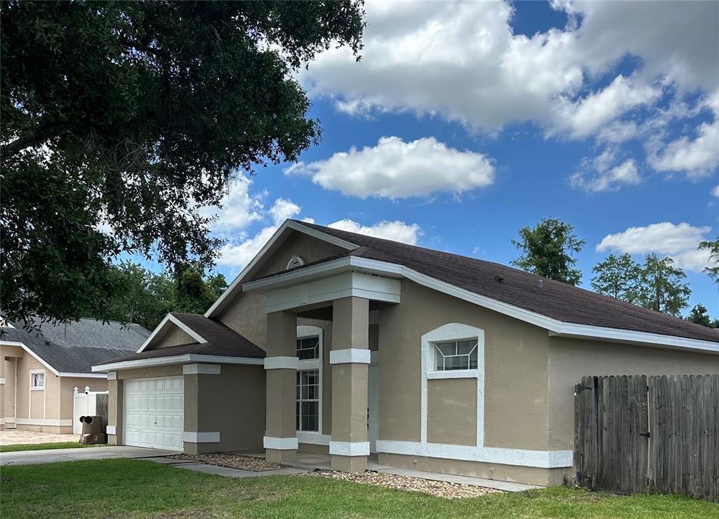 A tan single-story house with a white garage door, columns, and a wooden fence — 3119 FAIRFIELD DRIVE, KISSIMMEE, FL