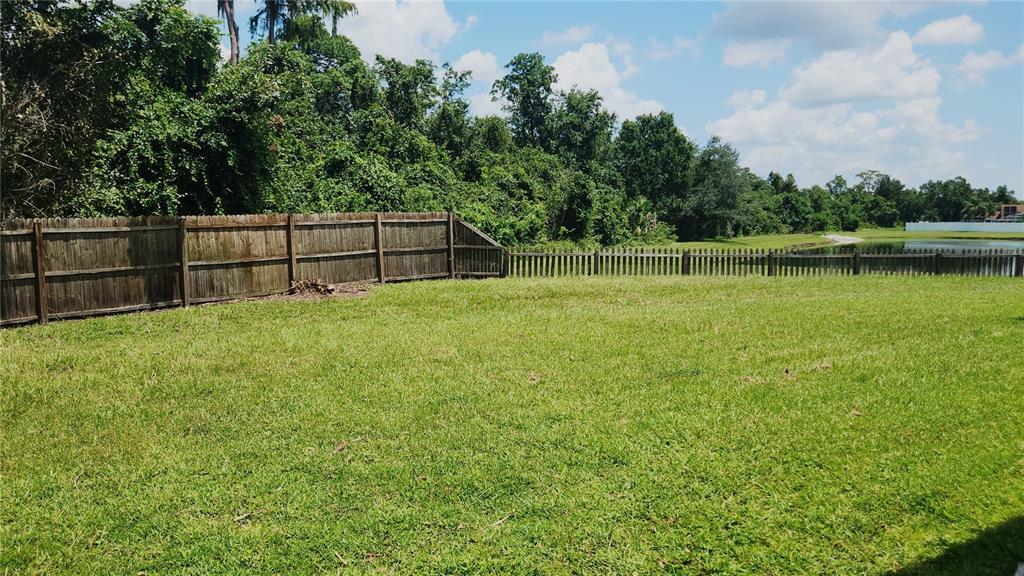 A grassy backyard features a wooden privacy fence and a view of a nearby pond — 3119 FAIRFIELD DRIVE, KISSIMMEE, FL