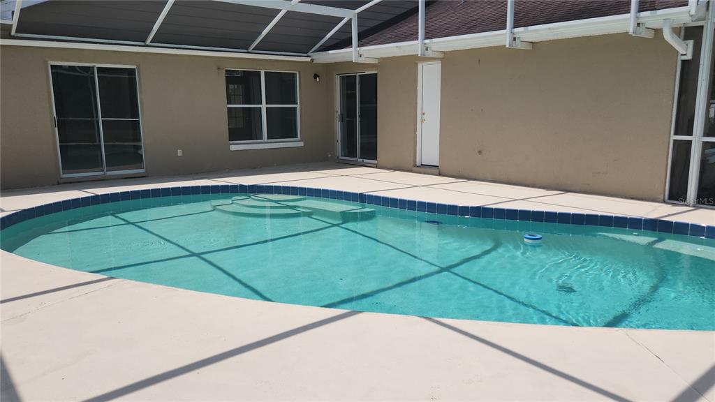 A grassy backyard with a screened pool enclosure, a wooden fence, and a pond view — 3119 FAIRFIELD DRIVE, KISSIMMEE, FL
