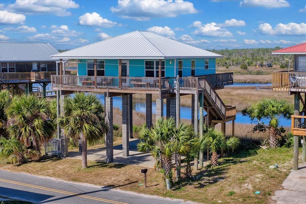 A bright blue stilt house with a metal roof overlooks a marshy landscape — 19018 GOOD TIMES DRIVE, PERRY, FL