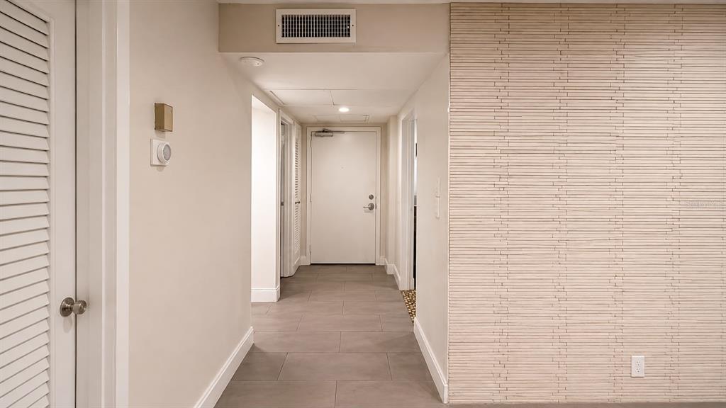 A hallway with gray tile flooring leads to a white door, featuring a textured accent wall — 8810 W MCNAB ROAD UNIT 303, TAMARAC, FL