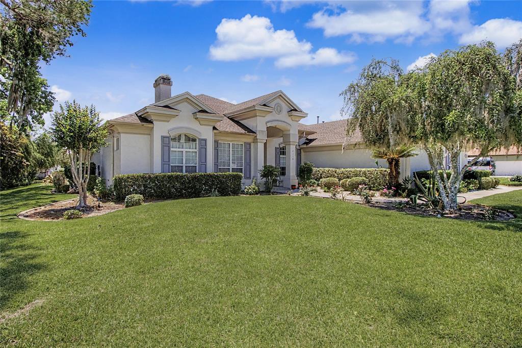 A single-story house with a light-colored stucco exterior, a front lawn, and mature trees — 2114 SE 25TH LOOP, OCALA, FL