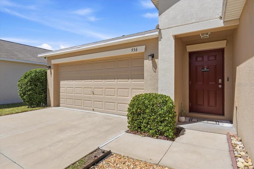 The exterior of a house features a tan garage, a red front door, and landscaping — 936 ZONE TAILED HAWK PLACE, RUSKIN, FL