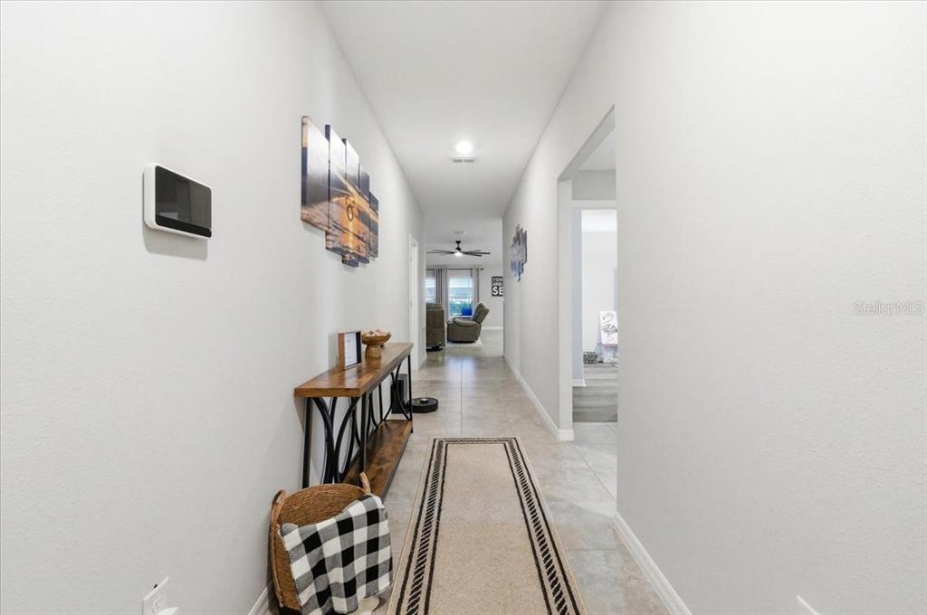 A hallway with light tile flooring, a console table, and wall art leads to a living area — 936 ZONE TAILED HAWK PLACE, RUSKIN, FL