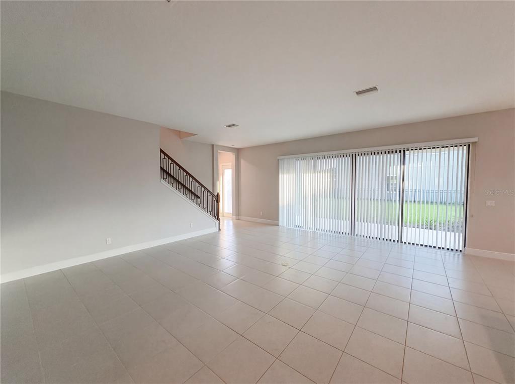 An open living area features light-colored tile flooring, a staircase with a dark railing, and sliding glass doors — 11277 RUSTIC TIMBER LOOP, SAN ANTONIO, FL