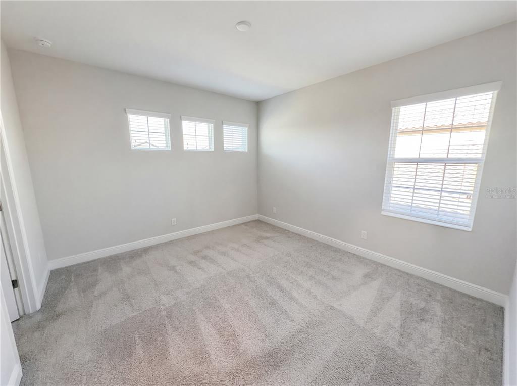 An empty bedroom features light gray walls, carpeted flooring, and several windows with blinds — 11277 RUSTIC TIMBER LOOP, SAN ANTONIO, FL