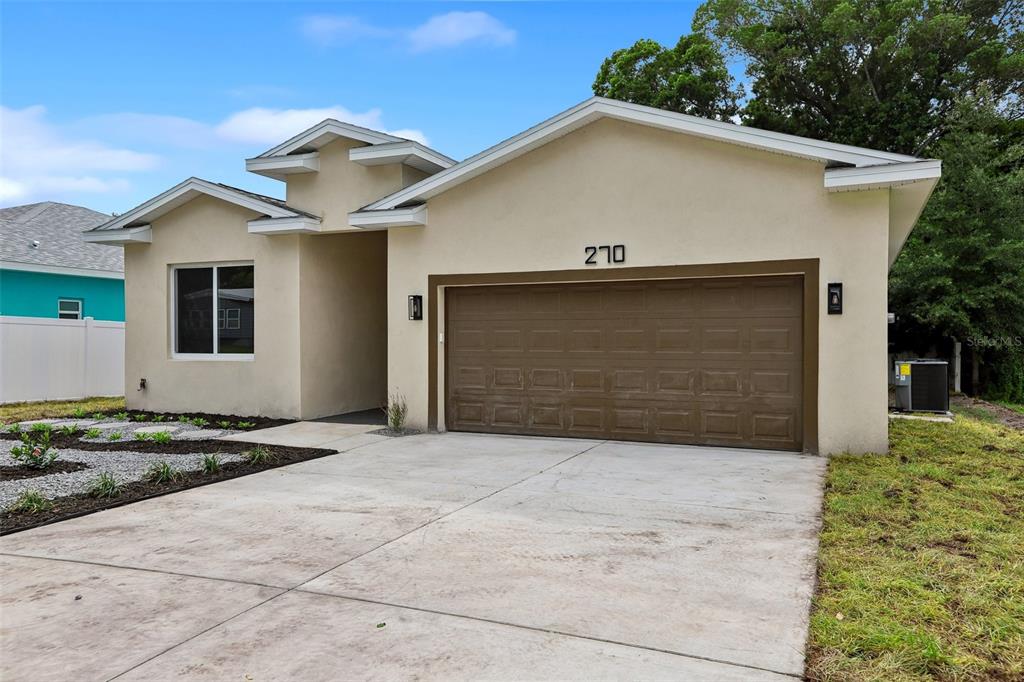 A single-story house with a beige stucco exterior, a brown garage door, and a concrete driveway — 270 DIOGENES STREET, DUNEDIN, FL