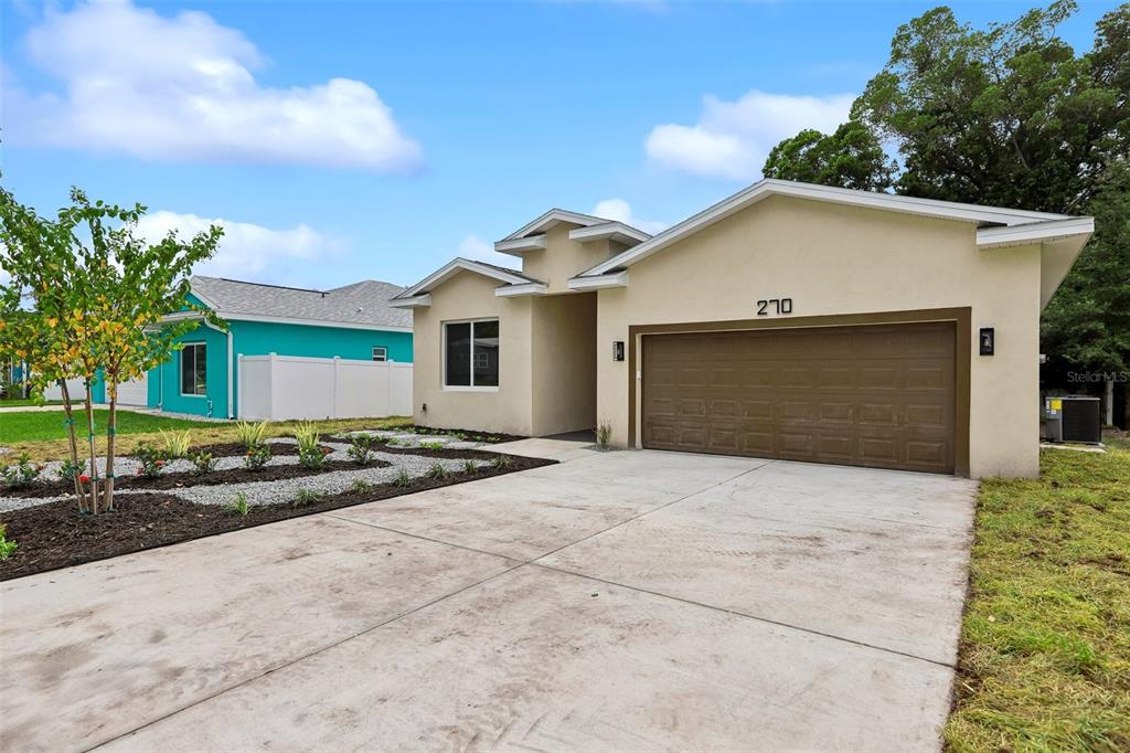 A tan single-story house with a brown garage door and a landscaped front yard — 270 DIOGENES STREET, DUNEDIN, FL