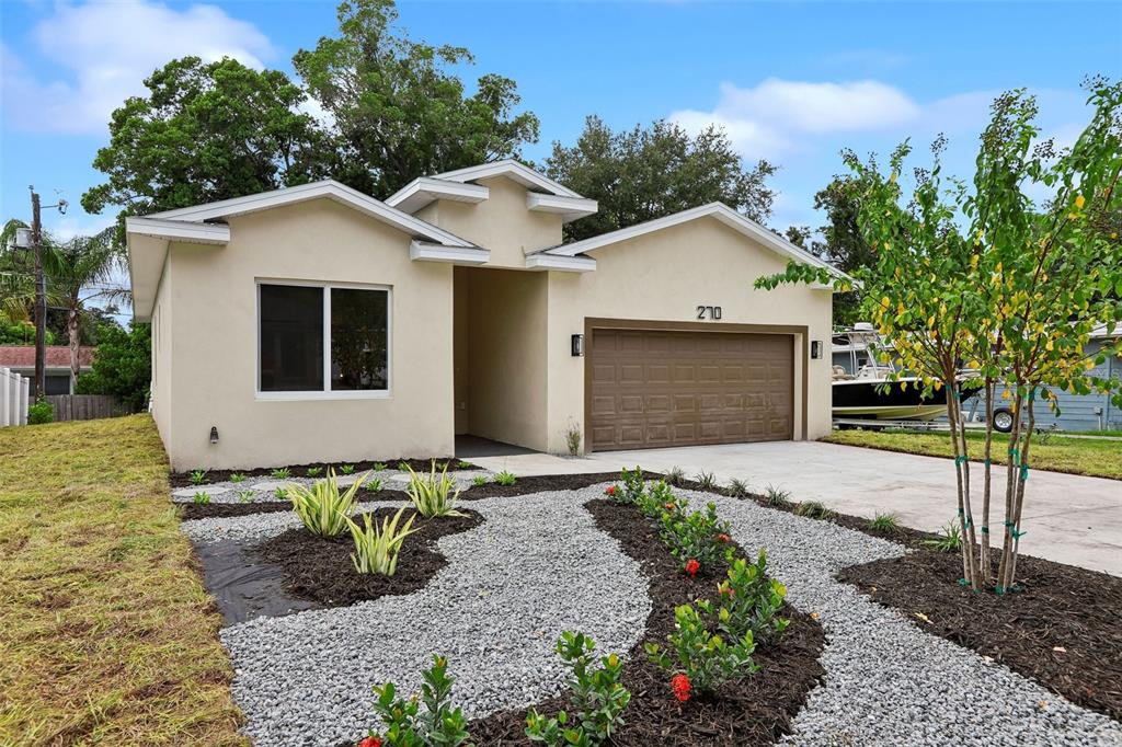 A single-story house with a beige stucco exterior, a two-car garage, and a landscaped yard — 270 DIOGENES STREET, DUNEDIN, FL