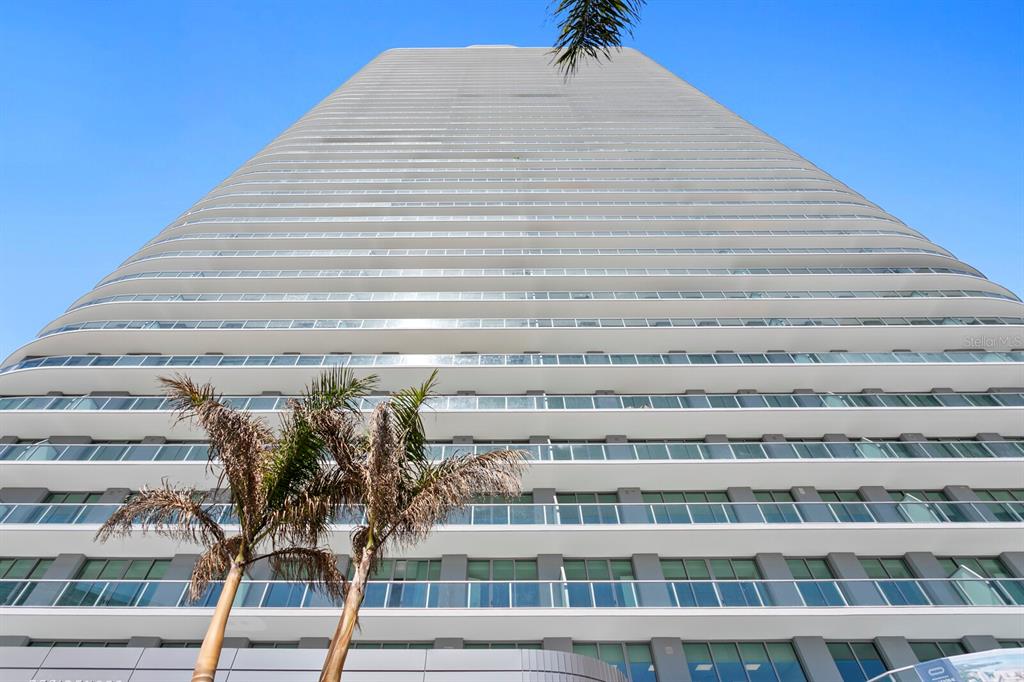 A low-angle view of a tall residential skyscraper with multiple balconies against a clear sky — 400 CENTRAL AVENUE UNIT 1704, ST PETERSBURG, FL
