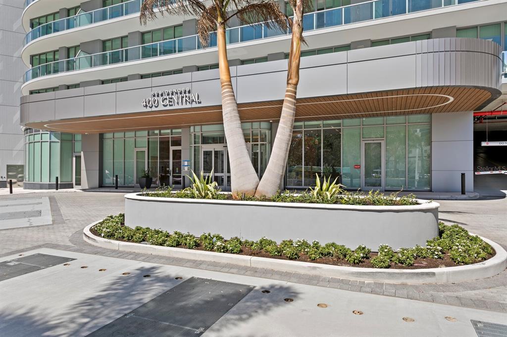 The exterior entrance of a modern residential building features a palm tree planter and glass facade — 400 CENTRAL AVENUE UNIT 1704, ST PETERSBURG, FL