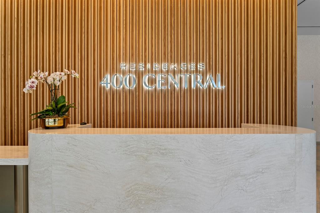 A modern reception desk sits in front of a vertical wood slat wall with signage — 400 CENTRAL AVENUE UNIT 1704, ST PETERSBURG, FL