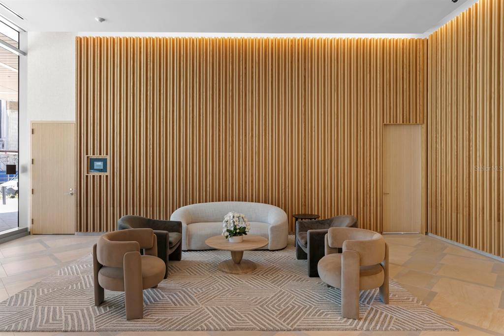A modern lobby features a curved sofa, armchairs, and a wood-slatted accent wall — 400 CENTRAL AVENUE UNIT 1704, ST PETERSBURG, FL