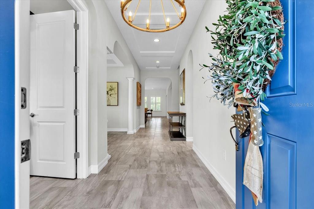 A bright entryway features gray wood-look tile flooring, a modern chandelier, and a blue door — 17923 BARN CLOSE DRIVE, LUTZ, FL