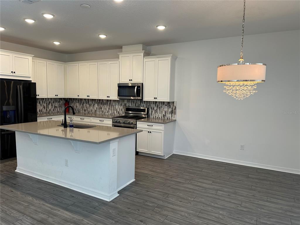 A modern kitchen features white cabinetry, gray countertops, a center island, and wood-look flooring — 1862 ISLAND VILLAGE WAY, CELEBRATION, FL