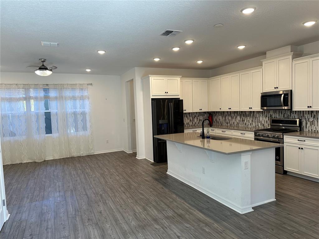A kitchen with white cabinets, a gray island, and wood-look flooring opens to a dining area — 1862 ISLAND VILLAGE WAY, CELEBRATION, FL