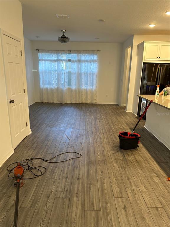 An open-concept room features wood-look flooring, a large window with white curtains, and a kitchen — 1862 ISLAND VILLAGE WAY, CELEBRATION, FL