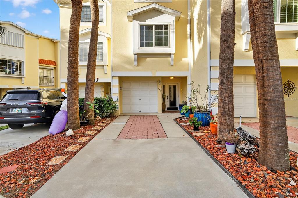 A yellow townhouse exterior features a concrete driveway, a brick walkway, and palm trees — 140 BRENT CIRCLE, OLDSMAR, FL