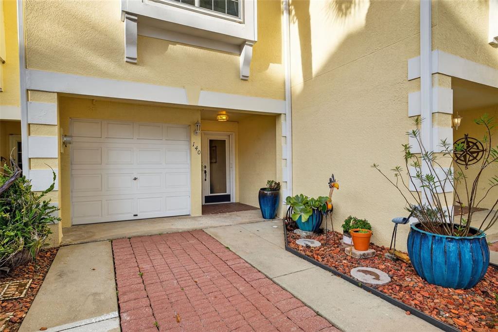 A yellow townhouse exterior features a white garage door, a front entrance, and potted plants — 140 BRENT CIRCLE, OLDSMAR, FL