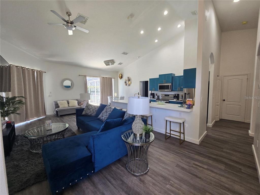An open-concept living room and kitchen feature blue furniture, wood-look flooring, and high ceilings — 751 BRUNELLO DRIVE, DAVENPORT, FL