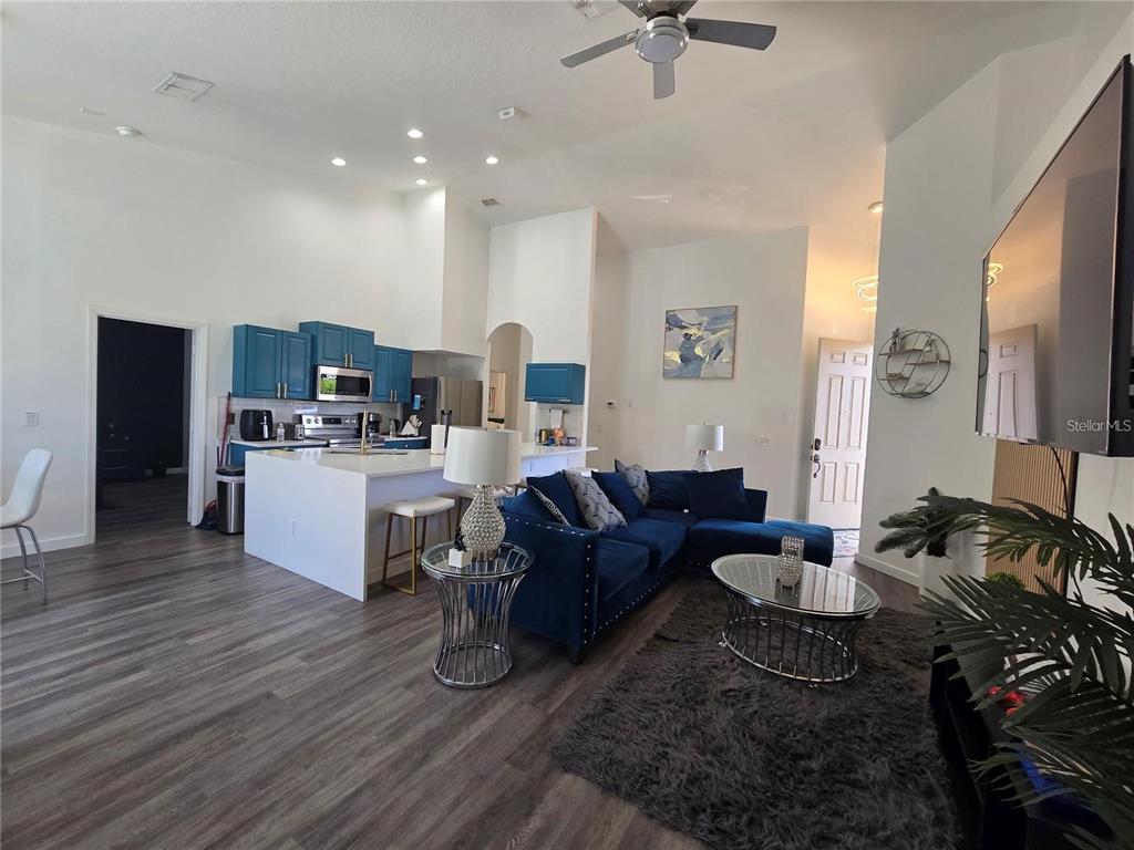 An open-concept living room features a blue sectional sofa, a kitchen island, and wood flooring — 751 BRUNELLO DRIVE, DAVENPORT, FL