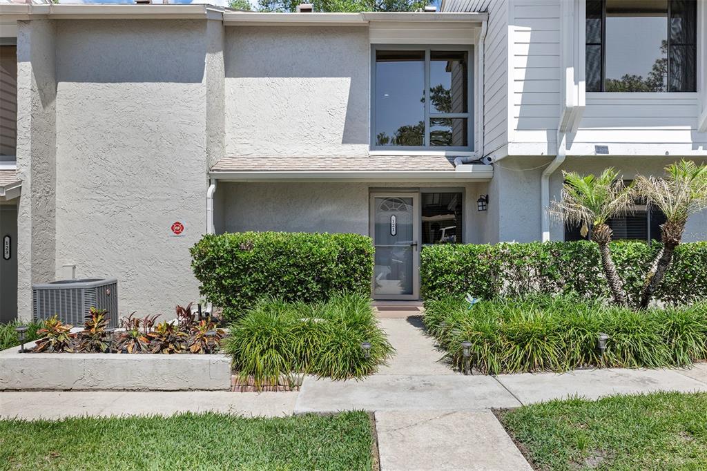 A two-story townhouse exterior features a concrete walkway, a front door, and landscaped bushes — 121 CROWN POINT CIRCLE UNIT 121, LONGWOOD, FL