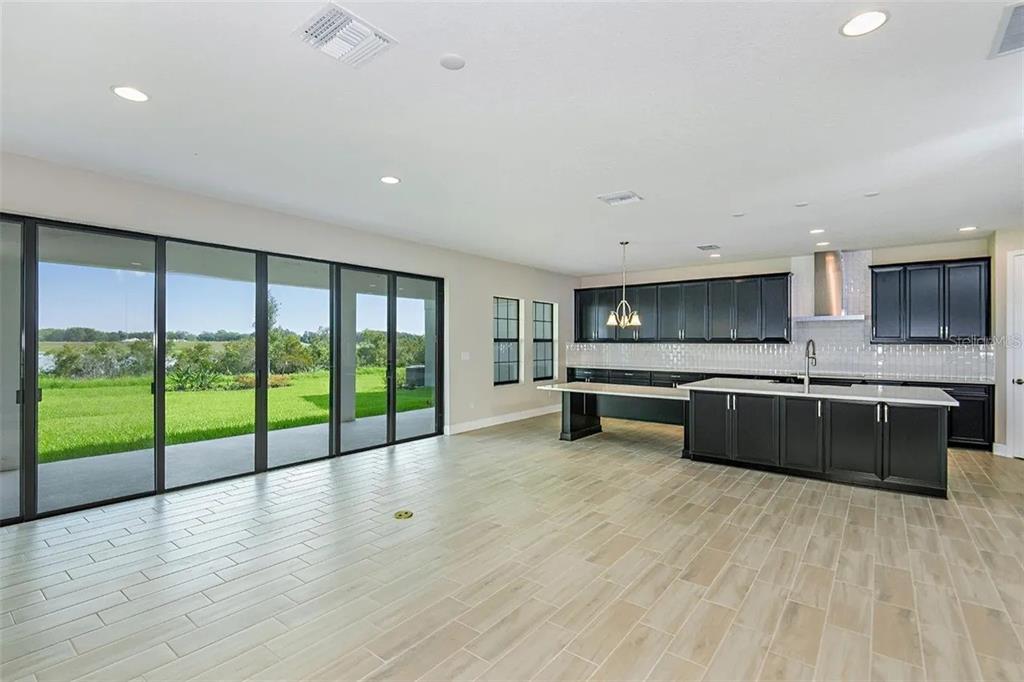 A modern kitchen with dark cabinets and a large island overlooks a grassy backyard through sliders — 12736 BERGSTROM BAY DRIVE, RIVERVIEW, FL