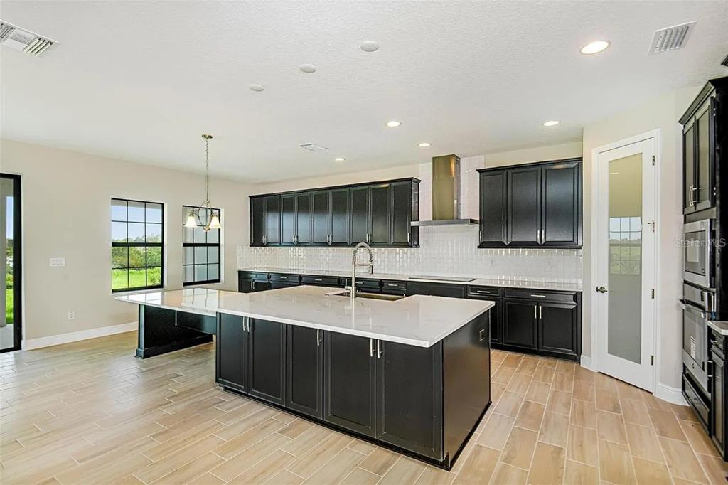 A kitchen with dark cabinets, a large white quartz island, and light wood-look tile flooring — 12736 BERGSTROM BAY DRIVE, RIVERVIEW, FL