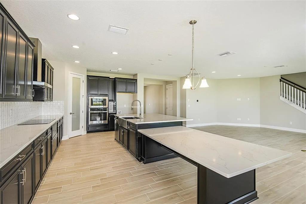 A modern kitchen features dark cabinets, light quartz countertops, a large island, and wood-look flooring — 12736 BERGSTROM BAY DRIVE, RIVERVIEW, FL