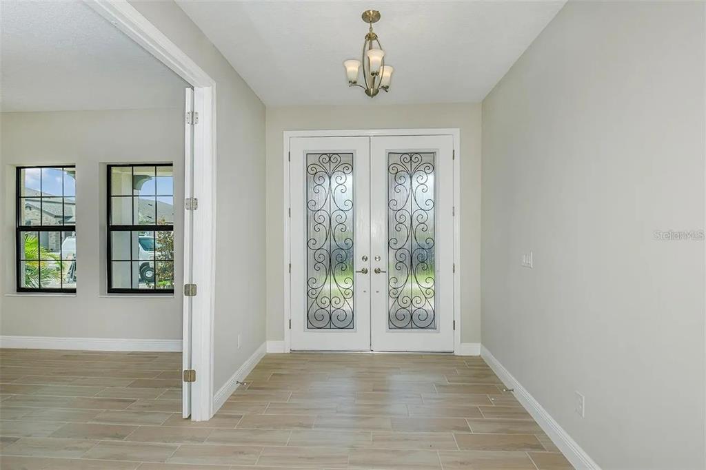 An entryway features double glass-paneled doors, light-colored tile flooring, and a small chandelier — 12736 BERGSTROM BAY DRIVE, RIVERVIEW, FL
