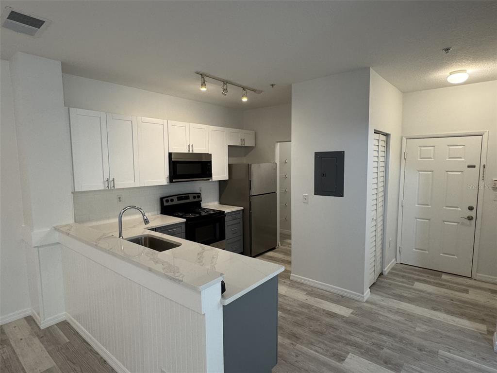 A kitchen features white upper cabinets, gray lower cabinets, stainless steel appliances, and wood-look flooring — 540 FLORIDA CLUB BOULEVARD UNIT 305, ST AUGUSTINE, FL