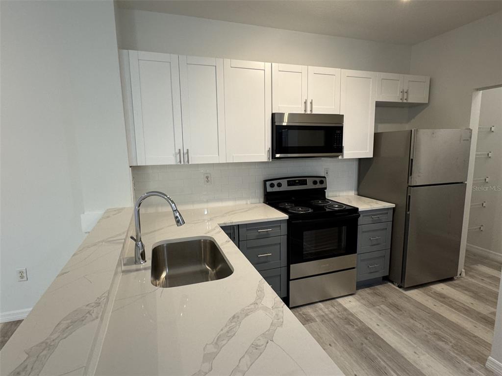 A kitchen features white upper cabinets, gray lower cabinets, stainless steel appliances, and quartz countertops — 540 FLORIDA CLUB BOULEVARD UNIT 305, ST AUGUSTINE, FL