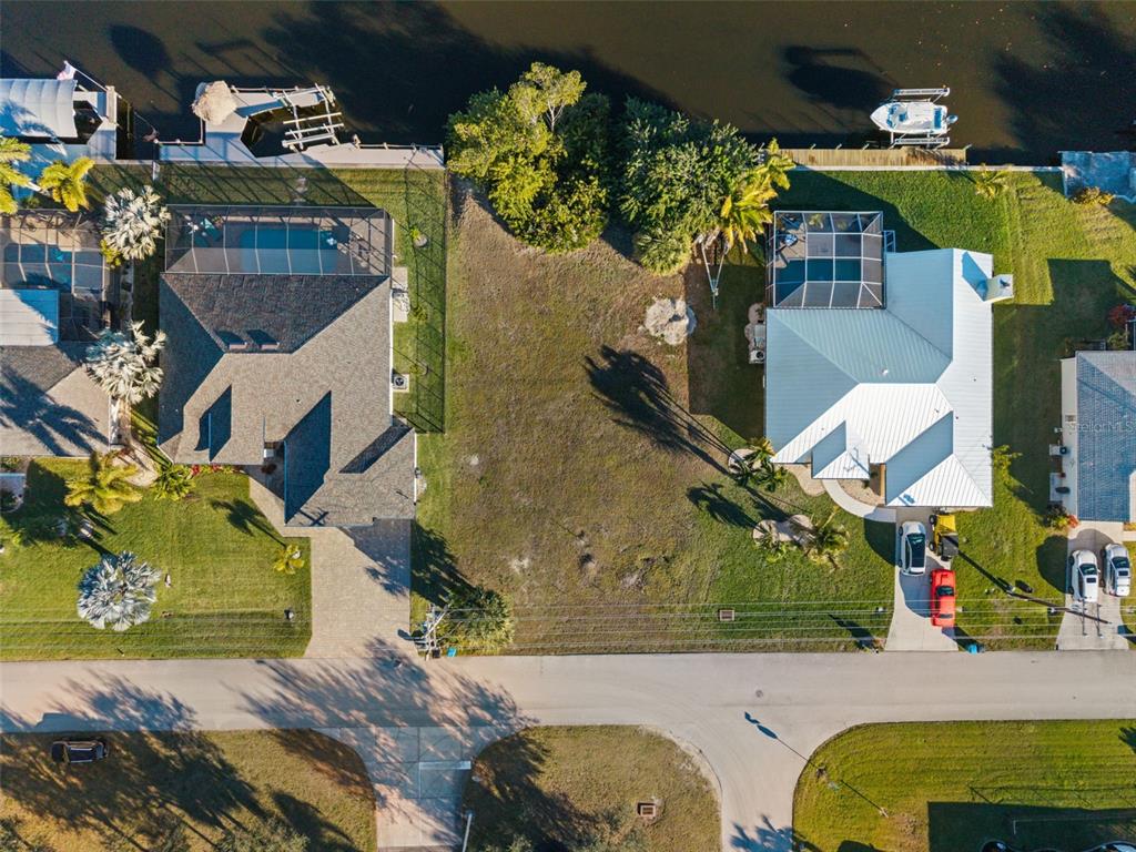 An aerial view shows a vacant waterfront lot situated between two houses with swimming pools — 241 SW 40TH STREET, CAPE CORAL, FL
