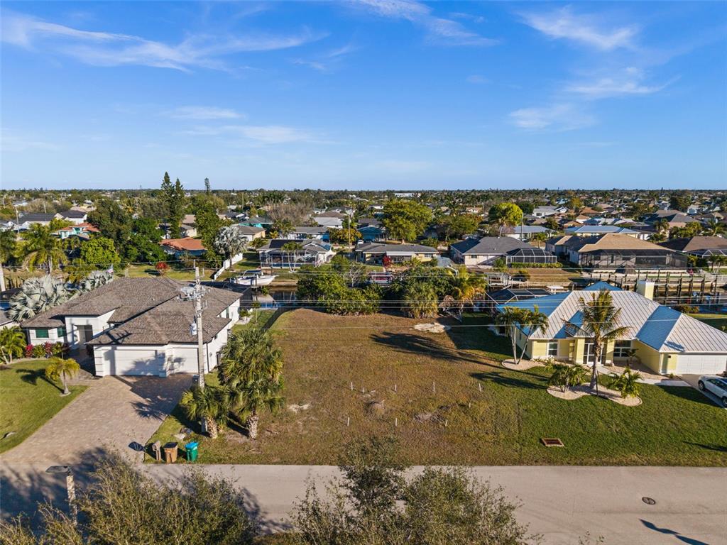 An aerial view shows a vacant residential lot situated between two houses near a canal — 241 SW 40TH STREET, CAPE CORAL, FL