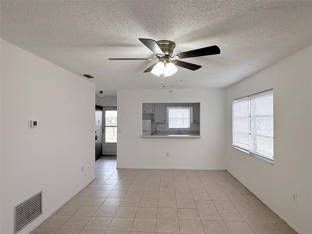 An empty room with tile flooring, a ceiling fan, and a pass-through to the kitchen — 390 301 BOULEVARD W UNIT 8D, BRADENTON, FL