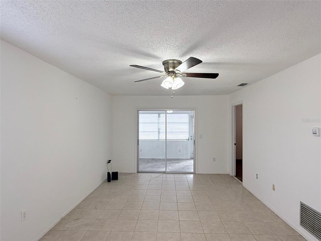 An empty room with white walls, tile flooring, a ceiling fan, and sliding glass doors — 390 301 BOULEVARD W UNIT 8D, BRADENTON, FL